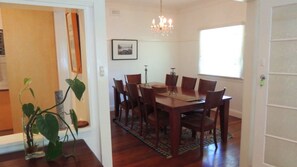 A dining area with a wooden table and chairs, a chandelier, and a window with blinds. - 52 Fingal Street by Lifestyle. Brunswick Heads (BRUNSWICK HEADS)
