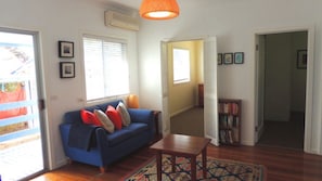 A living room with a blue sofa, a wooden coffee table, and a patterned rug. There is a bookshelf with books and a door leading to another room.