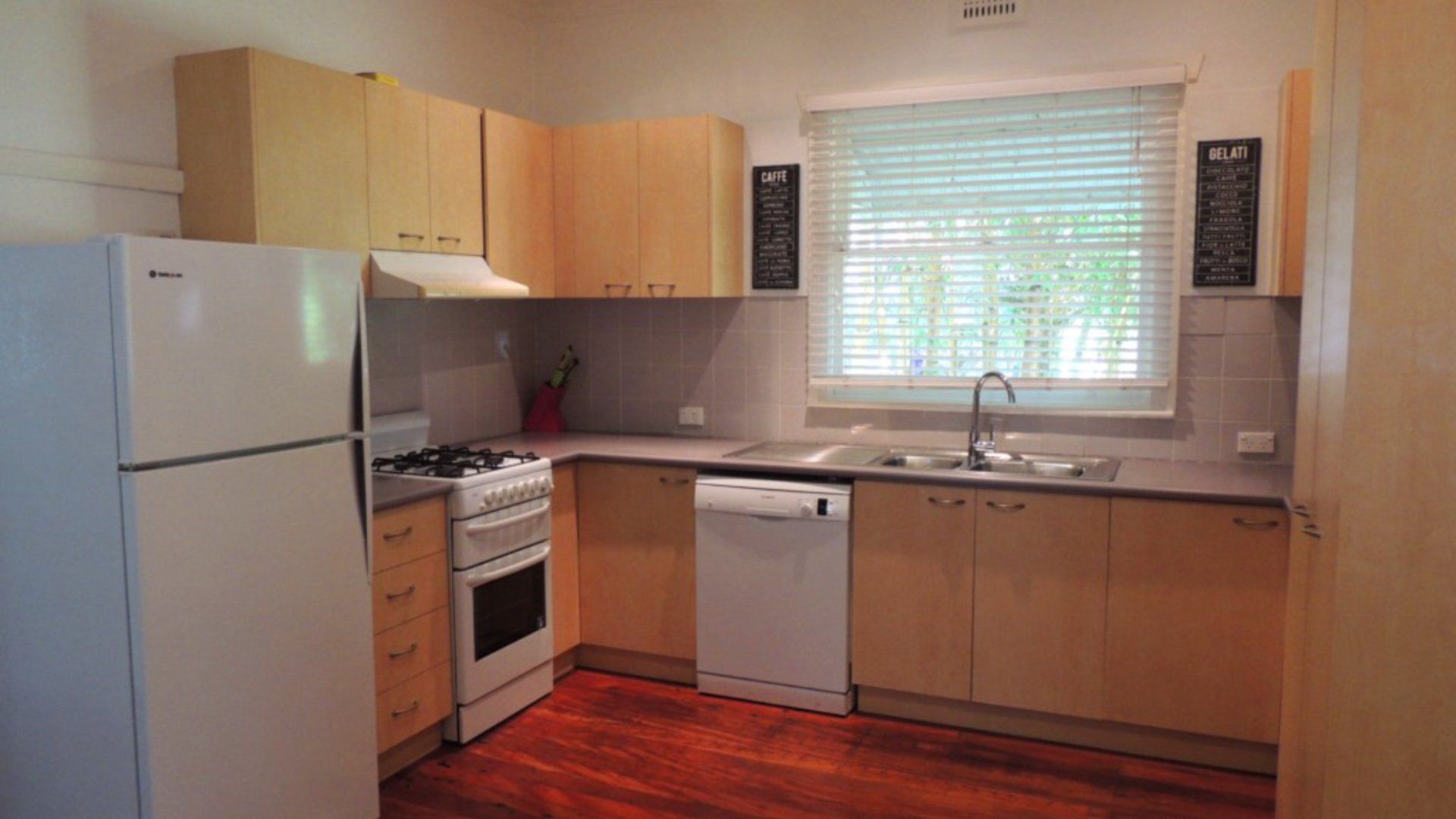 A compact kitchen with a refrigerator, stove, oven, dishwasher, and a window with blinds.