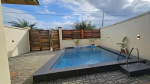 Una piscina rectangular con solárium alicatado, rodeada por una valla de madera y macetas con plantas.