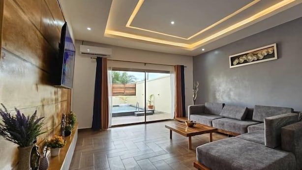 Una sala de estar moderna con un sofá gris, una mesa de centro de madera y un televisor de pantalla plana montado en la pared.
