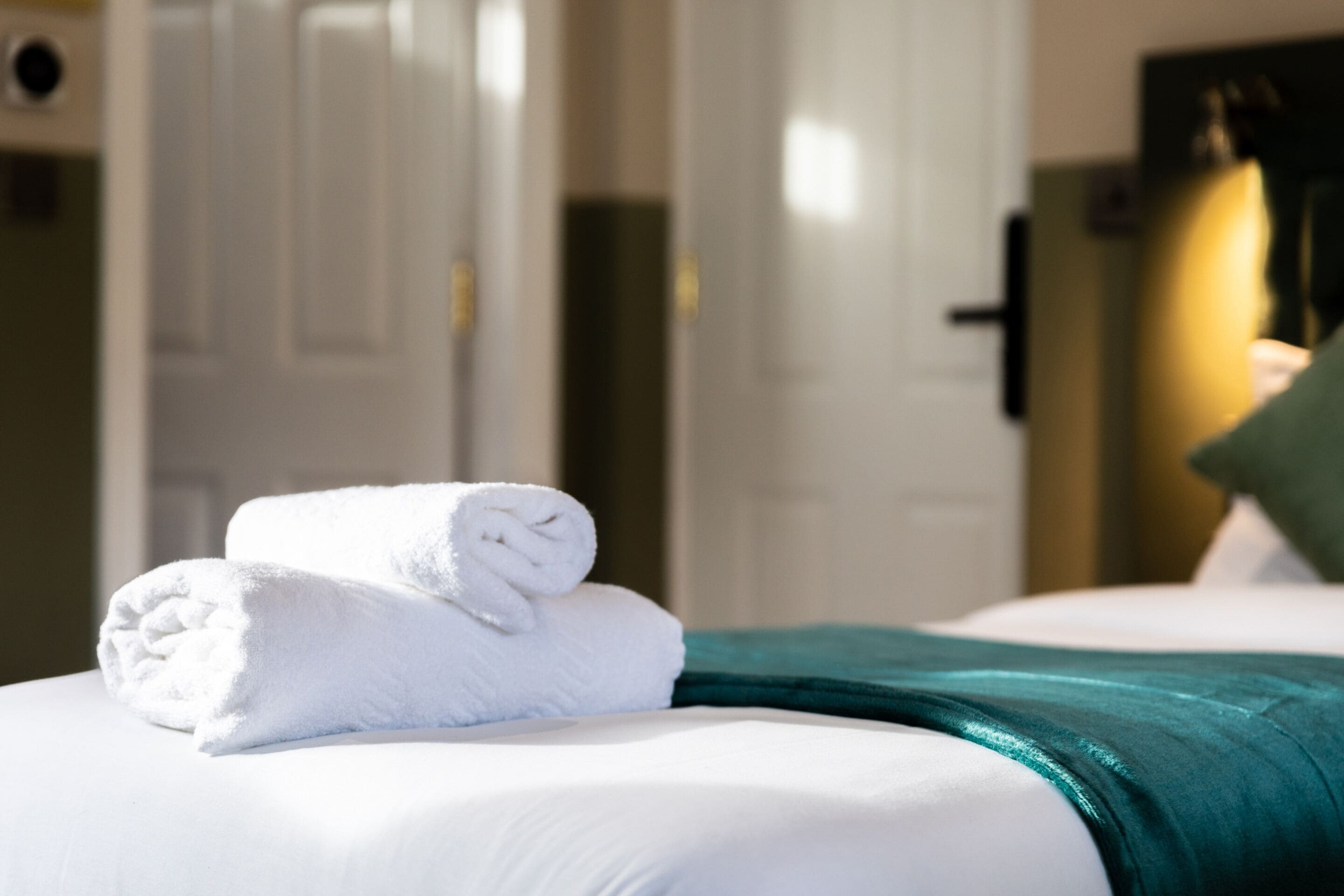 A neatly made bed with white linens and a teal throw blanket.