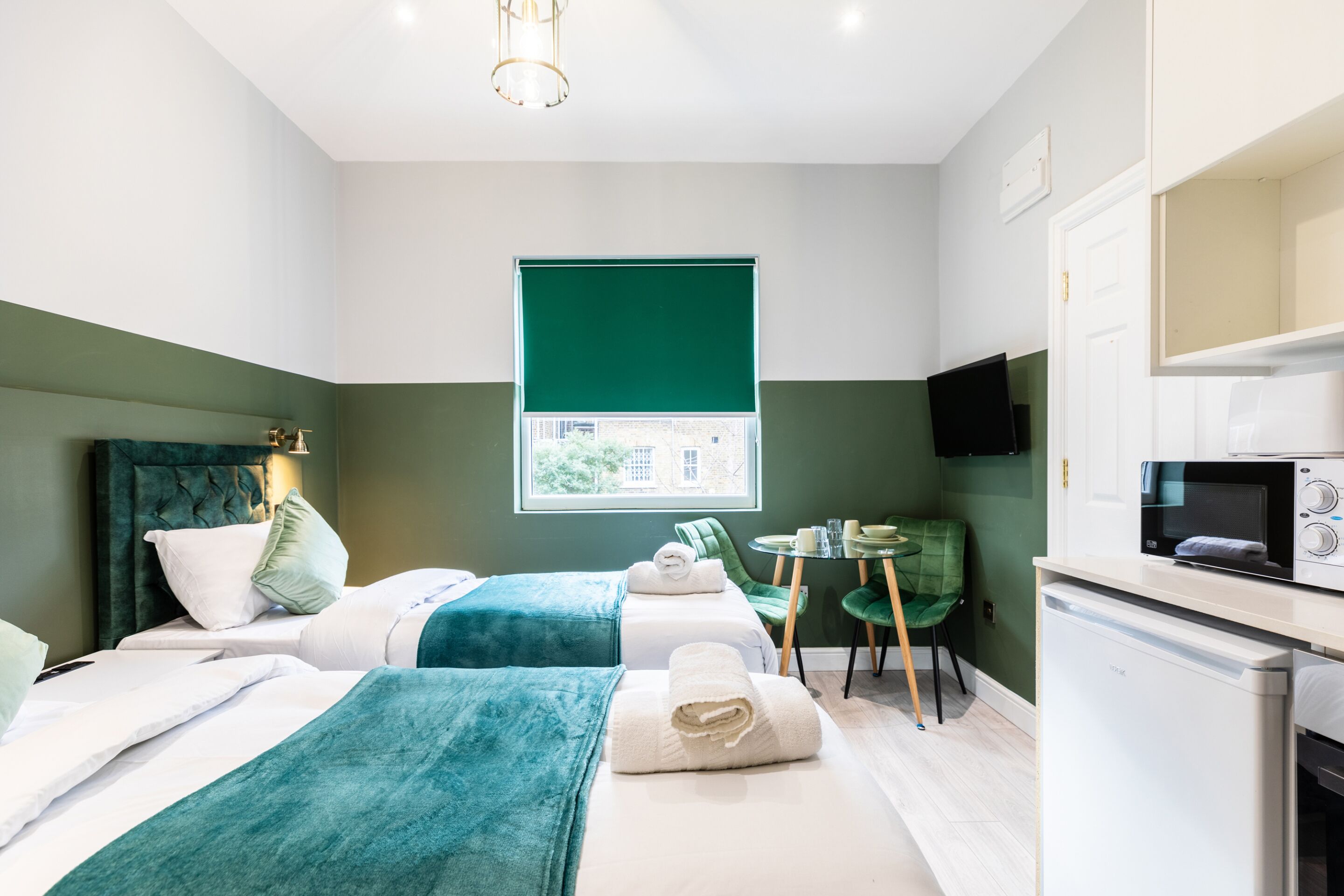 A hotel room with two beds, a small dining area, a microwave, and a TV.
