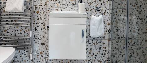Un baño con un lavamanos blanco, un espejo con iluminación y una ducha con puerta de vidrio, además de suelo de terrazo.