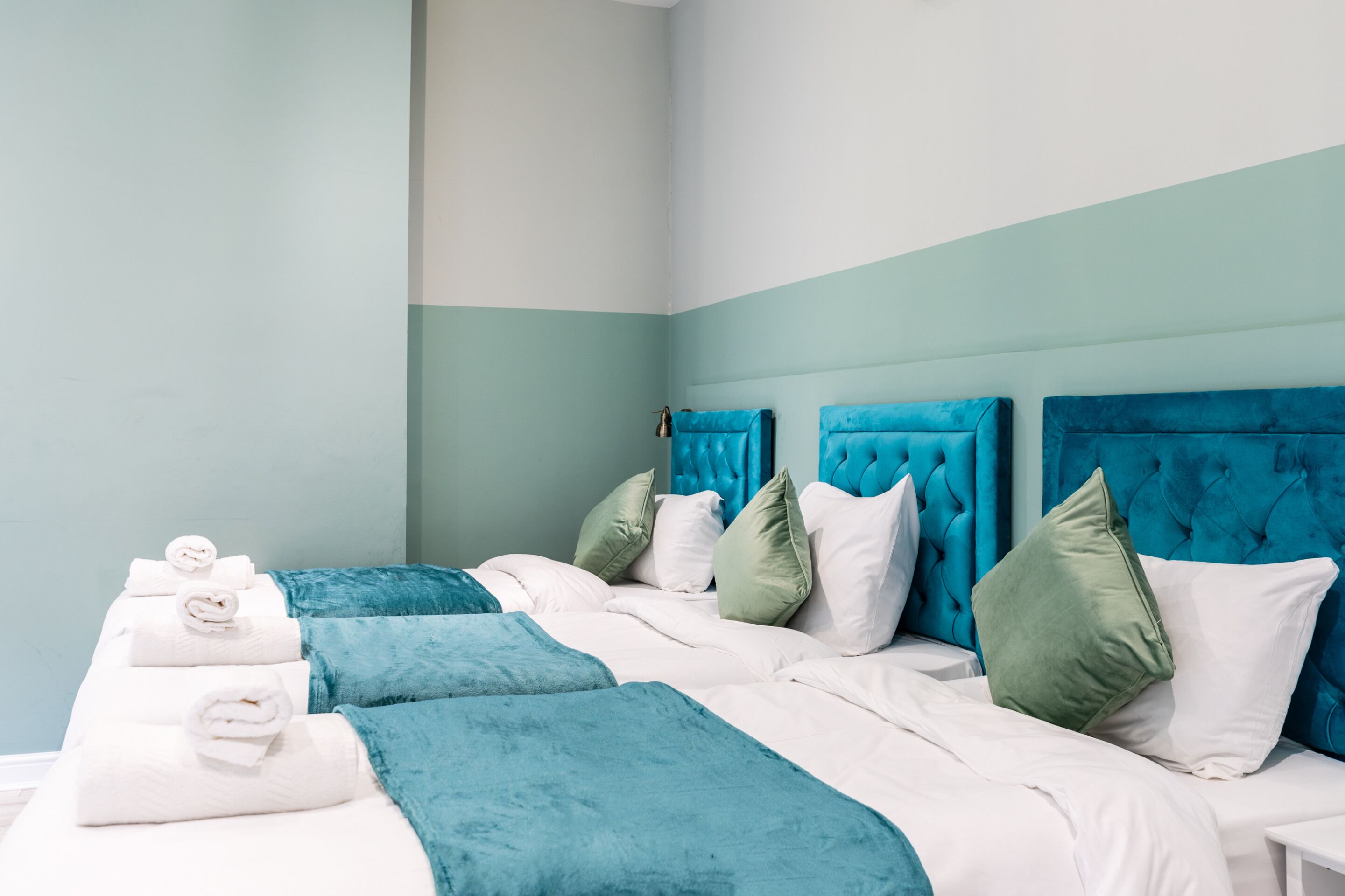 Una habitación de hotel con dos camas, ropa de cama azul verdosa y blanca, y cabecero azul verdoso.