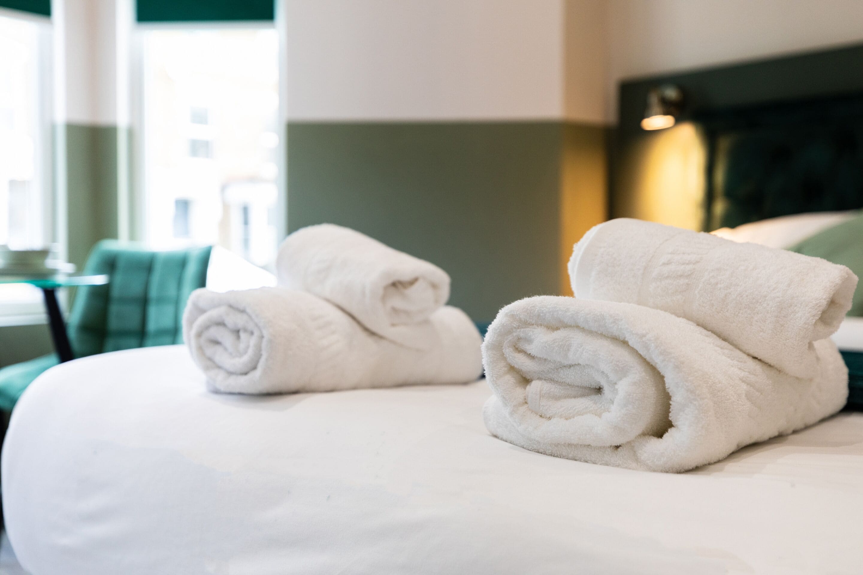A neatly made bed with two rolled white towels and a green and white striped pillow.