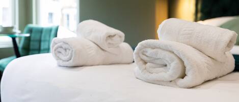 A neatly made bed with two rolled white towels and a green and white striped pillow.