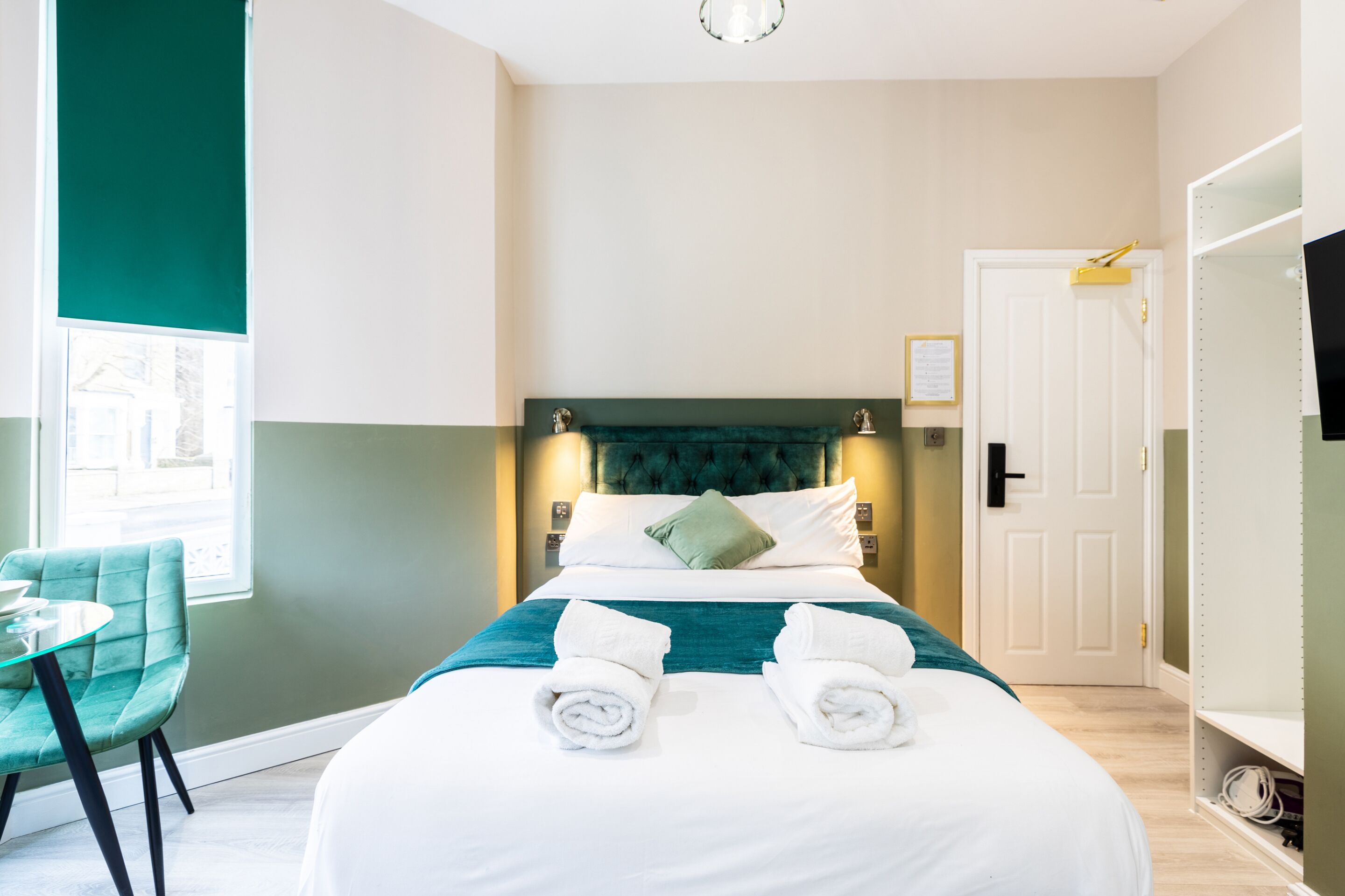 A hotel room with a bed, a chair, a desk, and a door.