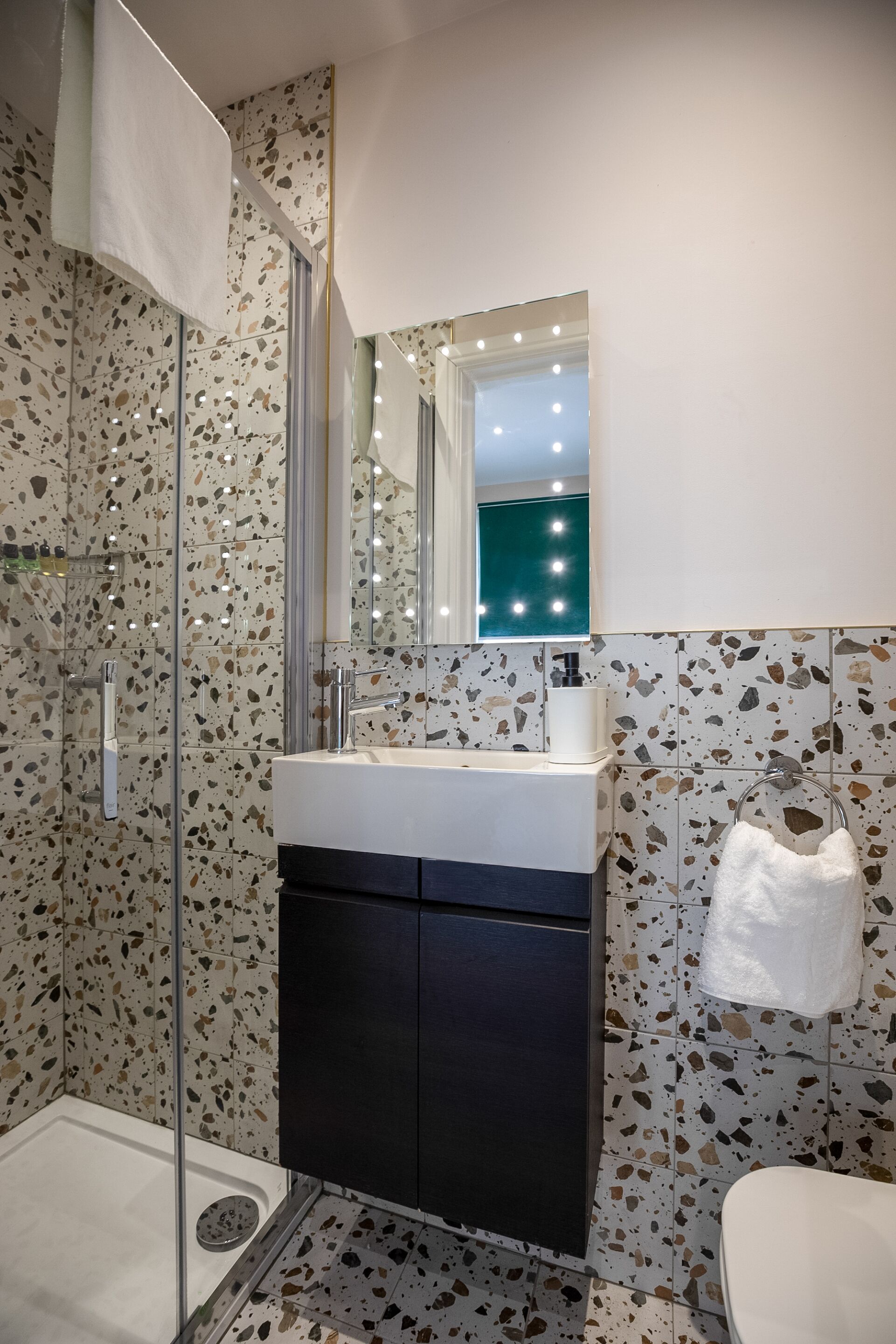 A modern bathroom with a glass shower enclosure, a white sink with a black cabinet, and a mirror with lights above it.