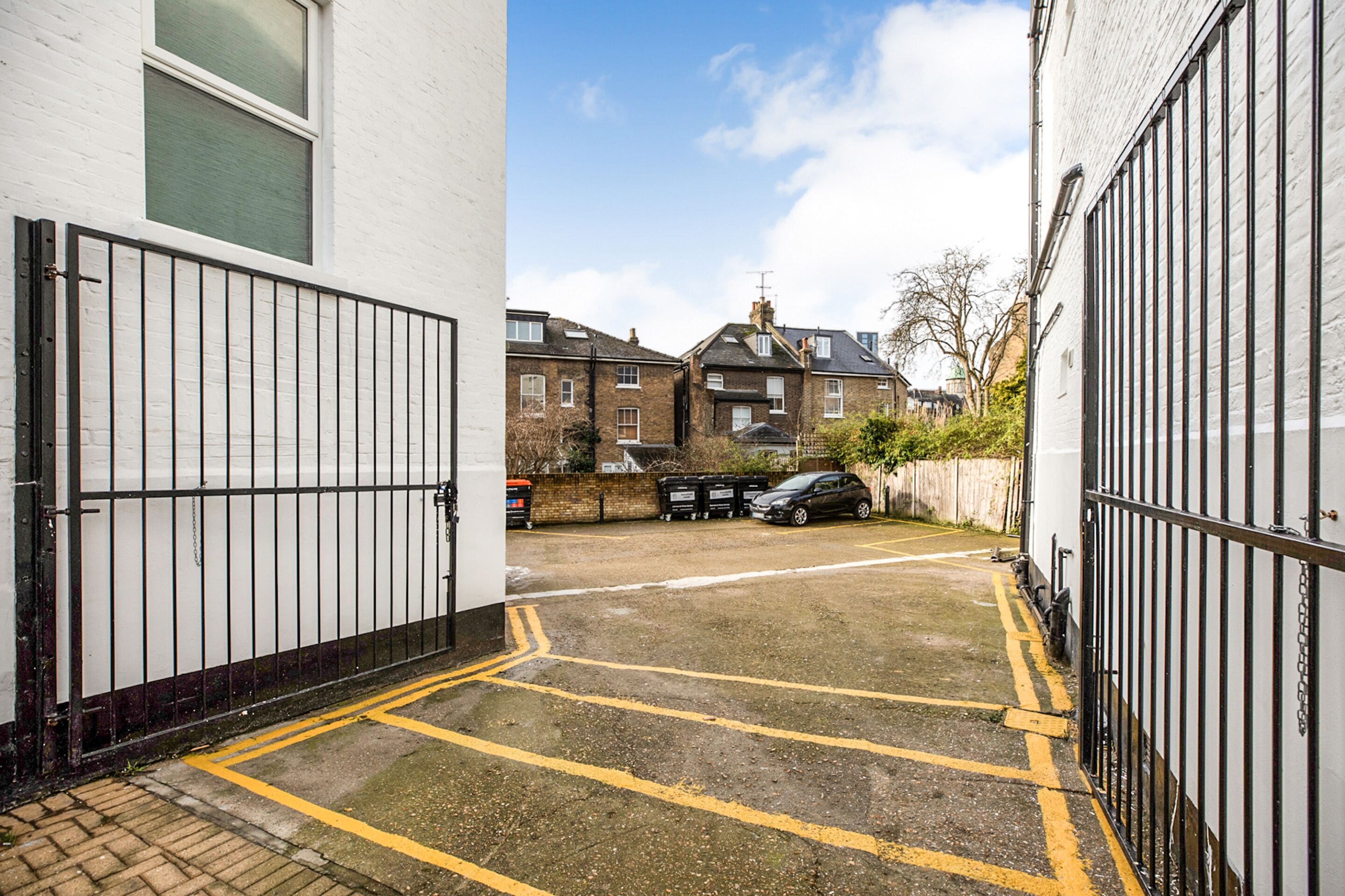 A narrow alleyway with a gated entrance, a parked car, and a building with a white facade.