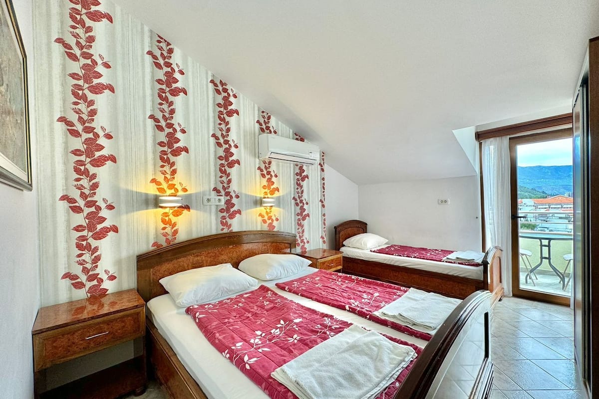 Une chambre d’hôtel avec deux lits, une tête de lit en bois, une table de chevet, une petite table et un balcon avec vue.