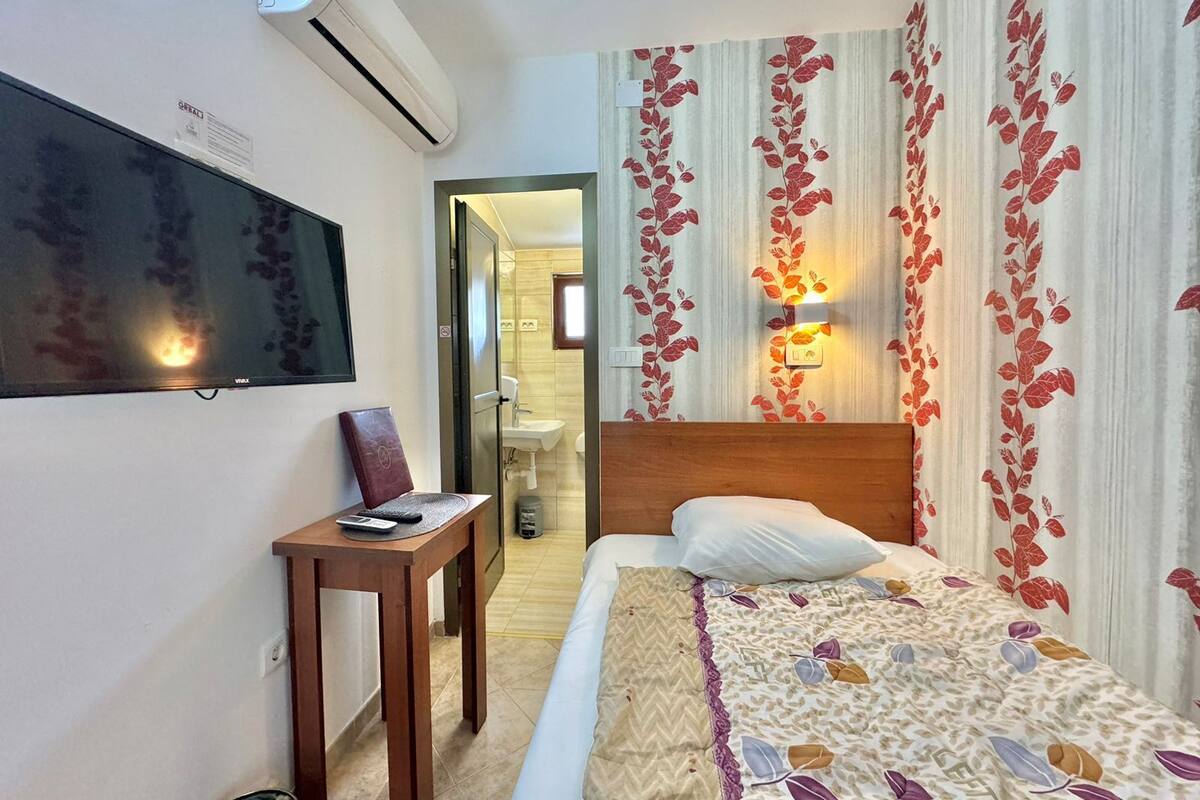 Une chambre d’hôtel avec un lit, un bureau, une télévision et une salle de bain visible à travers une porte ouverte.