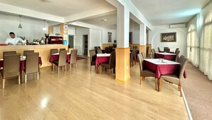 A restaurant with wooden flooring, red tablecloths, and a bar area with a chef preparing food. - Hotel Grbalj (Budva)