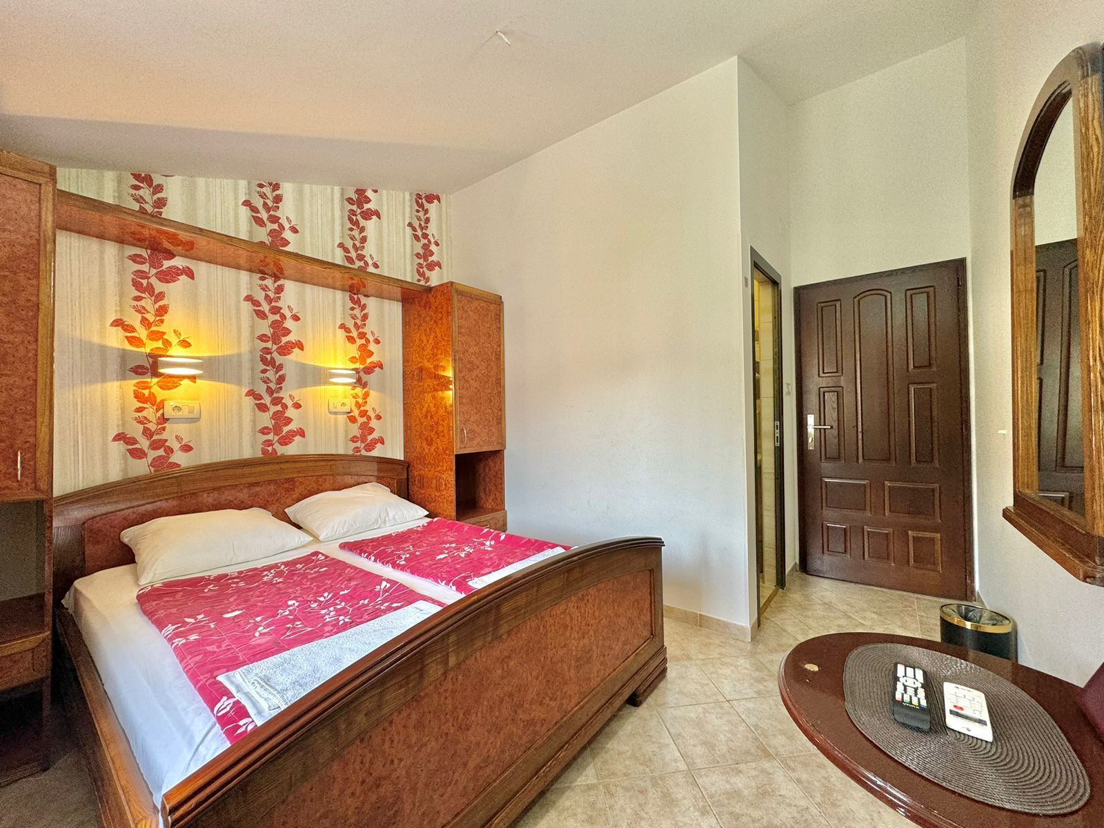 A double bed with a red and white bedspread, a wooden headboard, and two wall-mounted lamps.