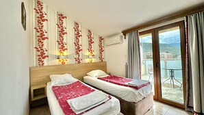 A hotel room with two beds, a balcony with a view of the sea, and a decorative wall with leaf patterns. - Hotel Grbalj (Budva)