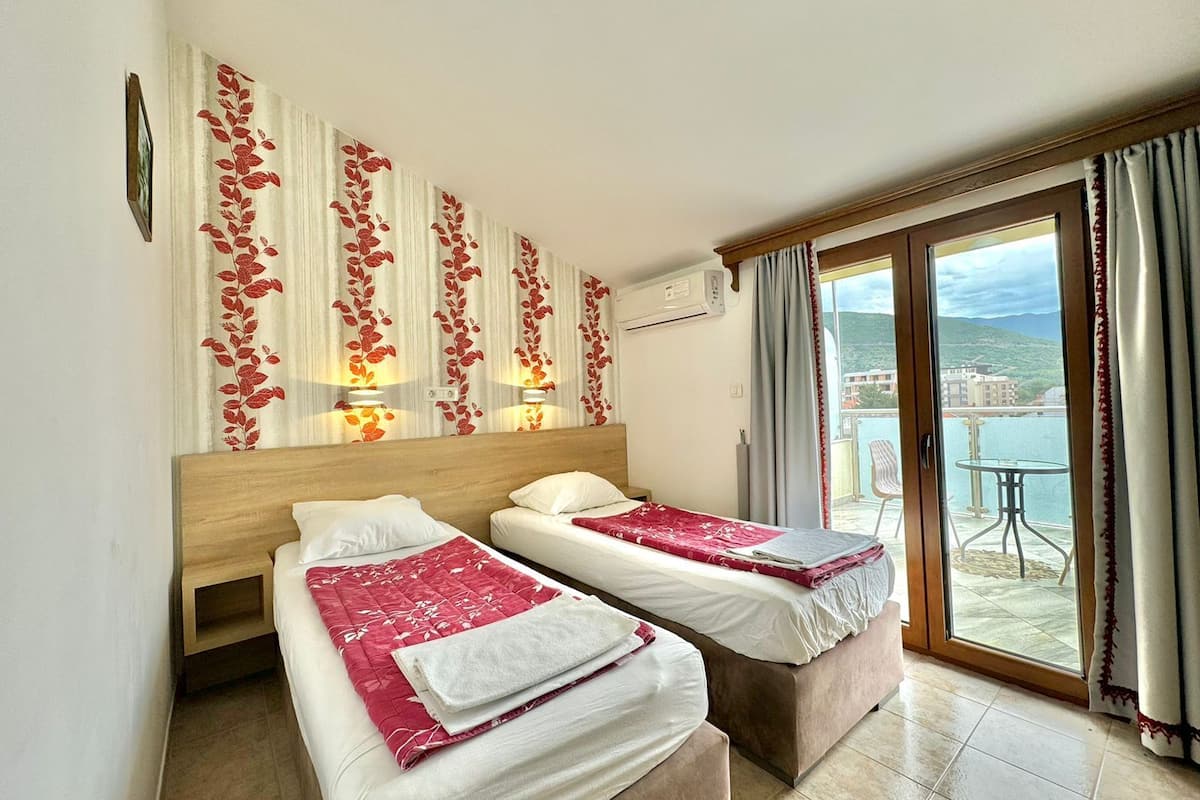 Une chambre d’hôtel avec deux lits, un balcon donnant sur la mer et un mur décoratif orné de motifs de feuilles.