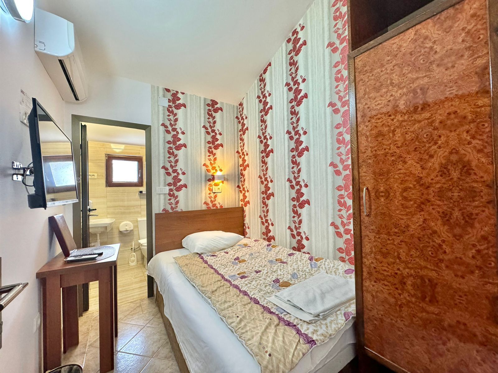 A hotel room with a bed, a desk, a wardrobe, and a bathroom visible through an open door.