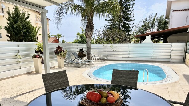 A poolside area with a round table, chairs, and a fruit basket. - STAY Villa Princess (Protaras)