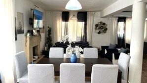 A dining area with a large table, striped chairs, a fireplace, and a television on the wall. - STAY Villa Princess (Protaras)