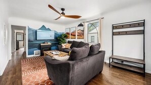 Un salon moderne avec un canapé gris, un plancher en bois, un ventilateur de plafond et un téléviseur fixé au mur.