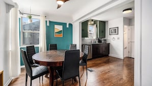 Un coin repas avec une table et des chaises en bois, un ventilateur de plafond et une vue sur la cuisine.