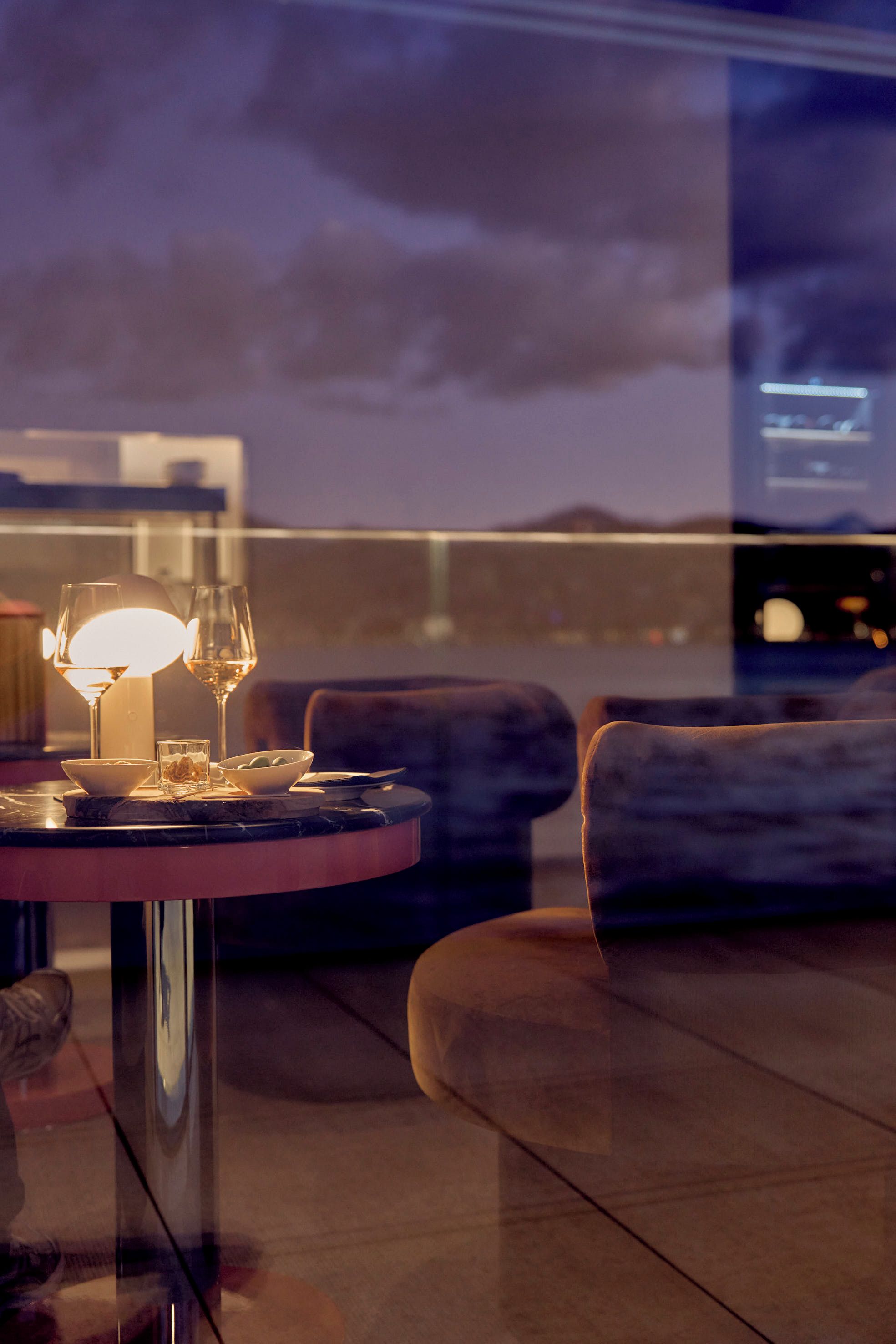 A dining table with a lamp, wine glasses, and a bowl of olives.