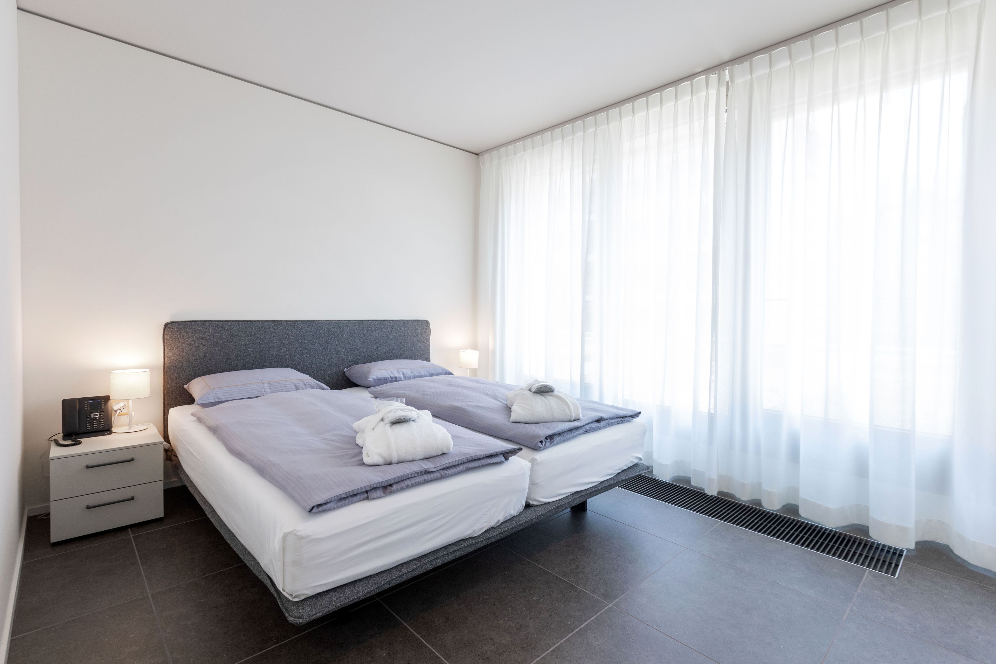 Ein modernes Hotelzimmer mit einem großen Bett, Nachttischen und einem Fenster mit durchsichtigen Vorhängen.