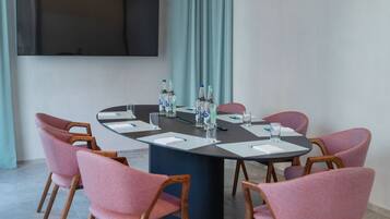 Une salle de conférence moderne, dotée d’une table ronde, de chaises rembourrées de couleur rose et d’un grand téléviseur à écran plat fixé au mur.