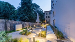A courtyard with a paved walkway, benches, an umbrella, and a wall with a metal railing. - Residenza Du Lac (Paradiso)