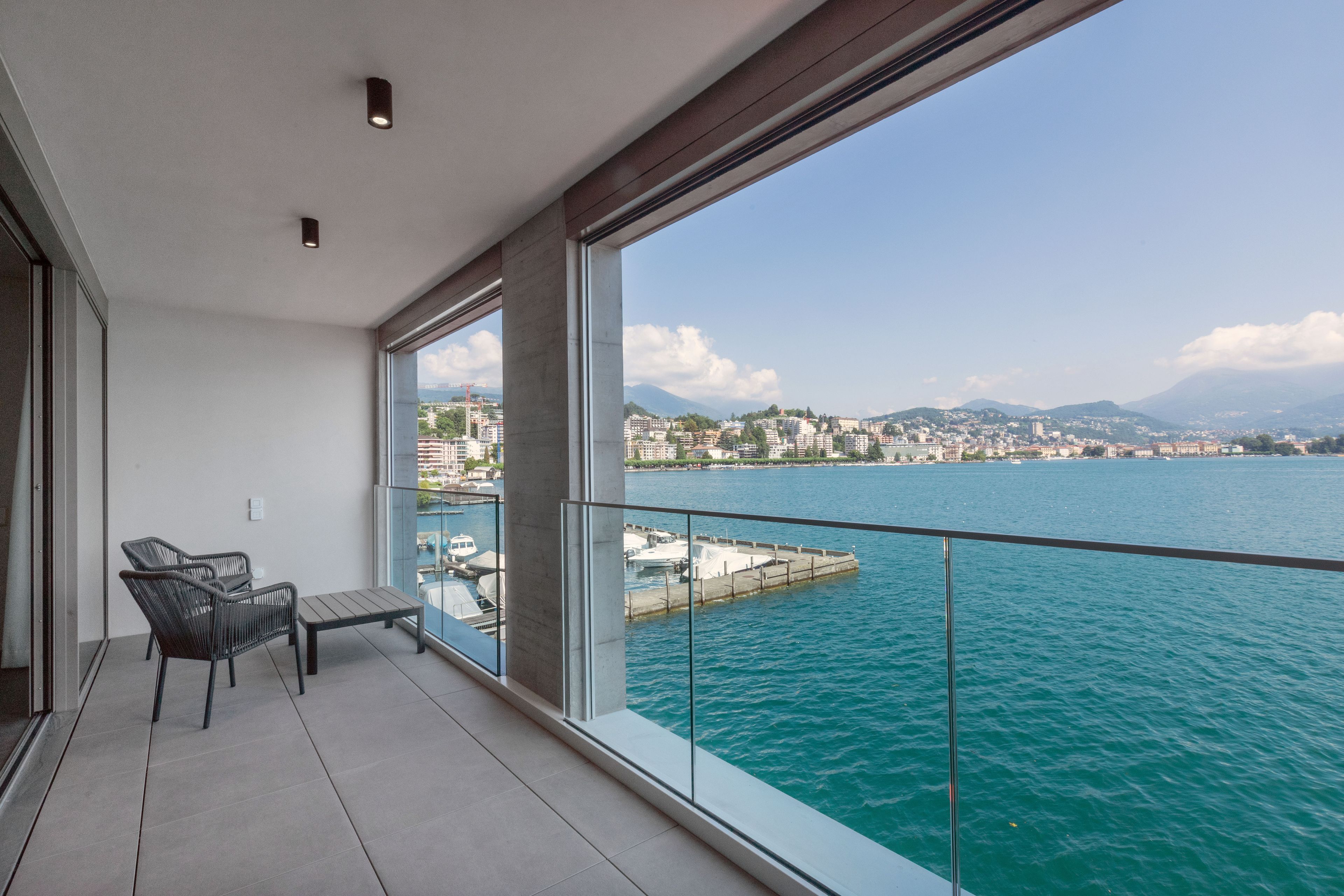 A balcony with a view of a lake and cityscape, featuring a seating area and large windows.