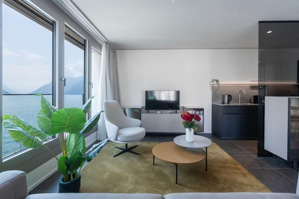A modern living room with a sofa, a coffee table, a TV, and a kitchen area.