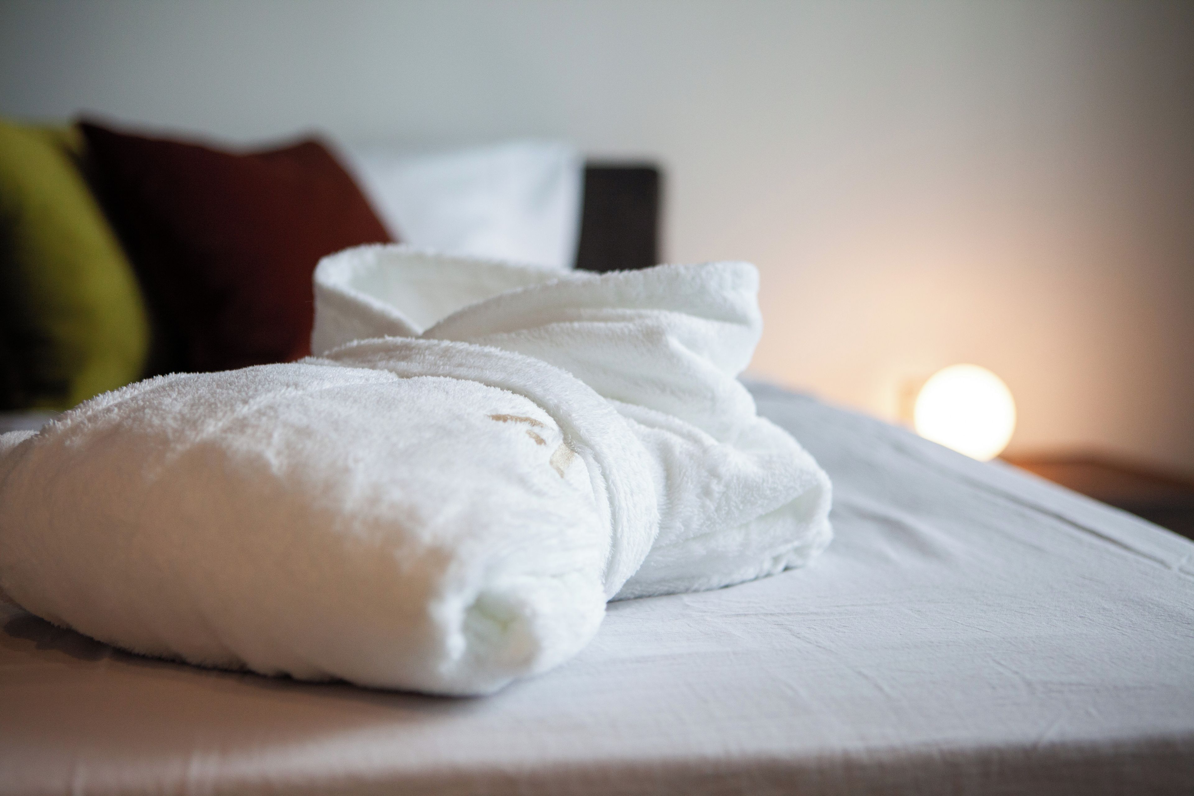 Una cama bien tendida con sábanas blancas y dos toallas enrolladas encima.