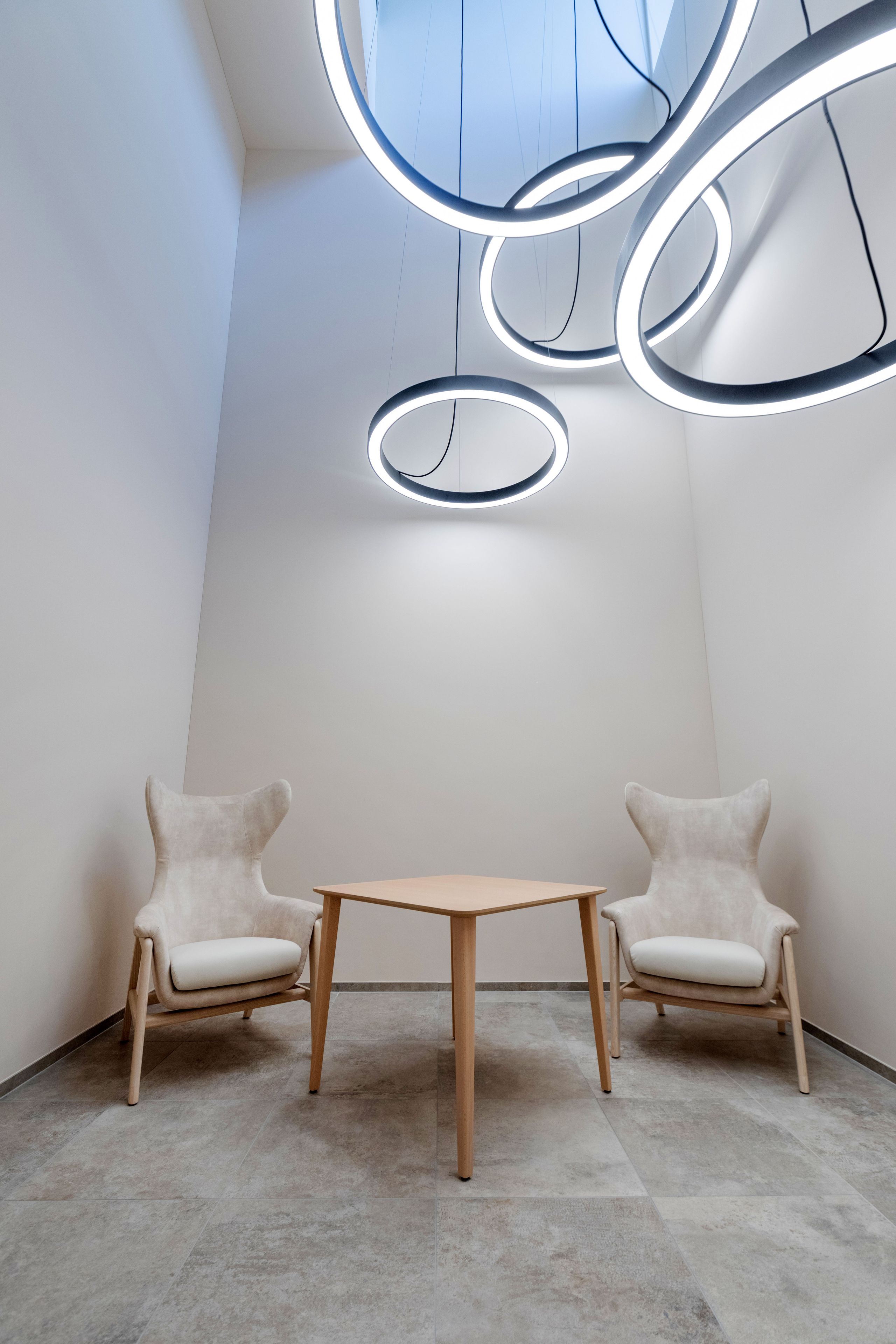 Une pièce moderne au design minimaliste, comprenant une table en bois et deux chaises rembourrées, un luminaire aux formes géométriques et un mur blanc uni.