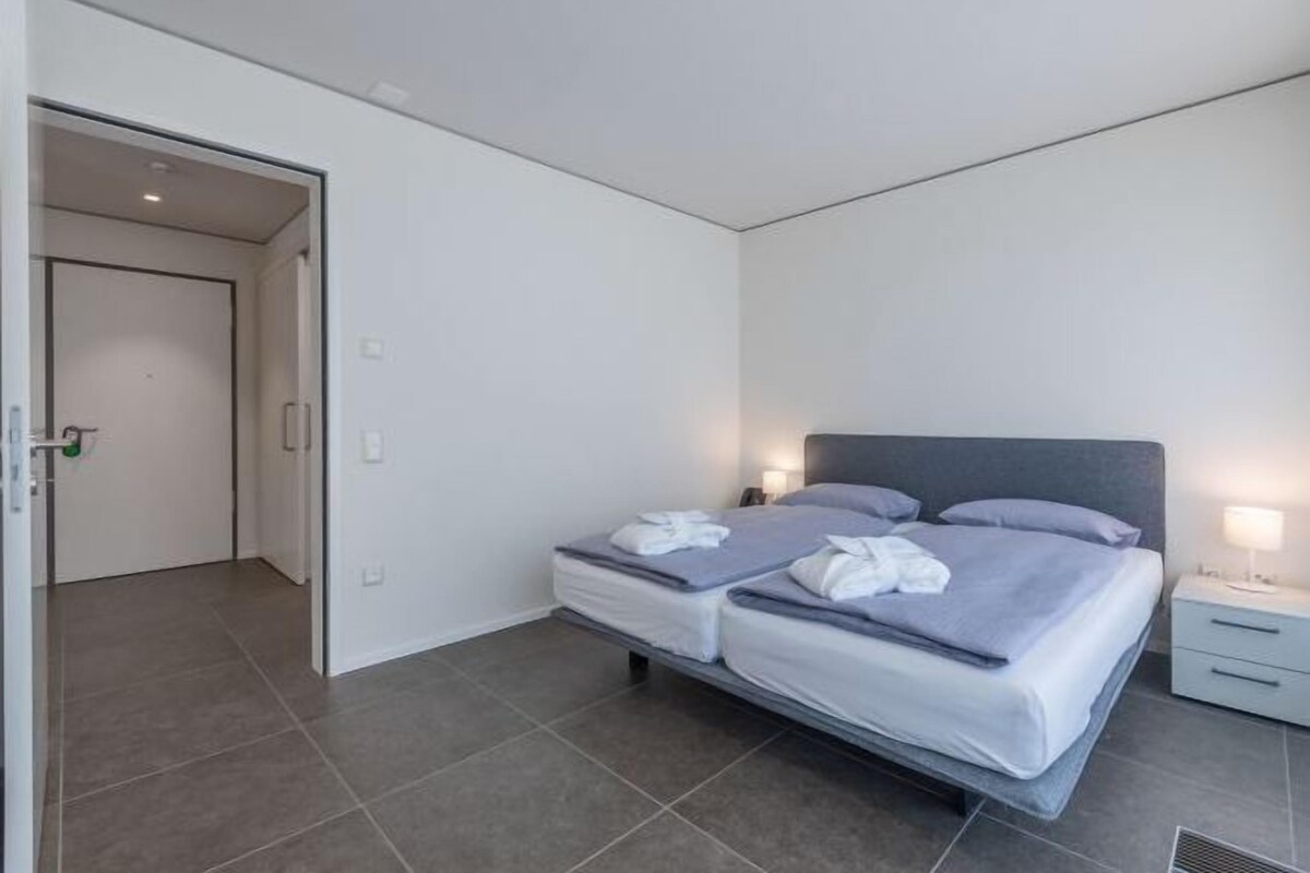 A modern bedroom with a bed, bedside tables, and a door leading to another room.