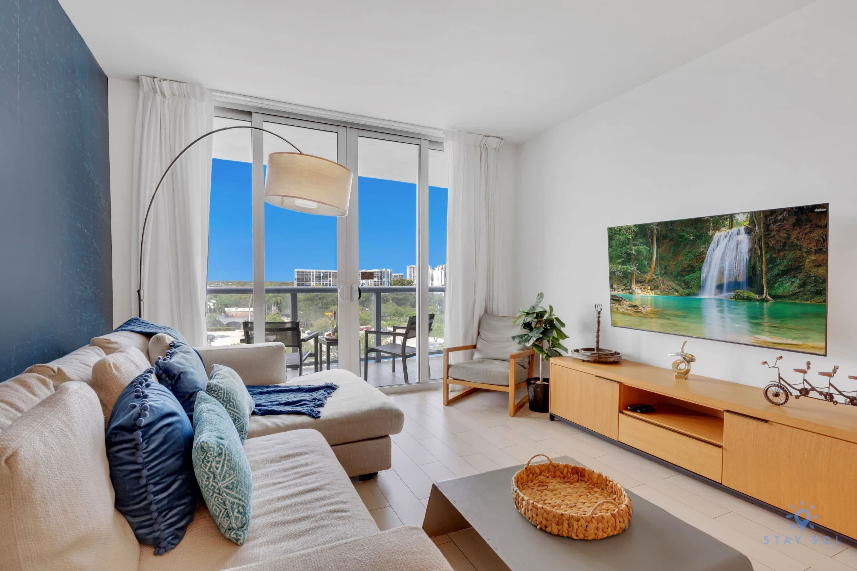 Un salon moderne avec un canapé, une télévision et un balcon offrant une vue sur la ville.