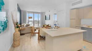 A modern apartment with a central island kitchen, a dining area, and a living room with a sofa and a large window. - Infinite View| Balcony+ Amazing Pool+ Near Beach (Hallandale Beach)