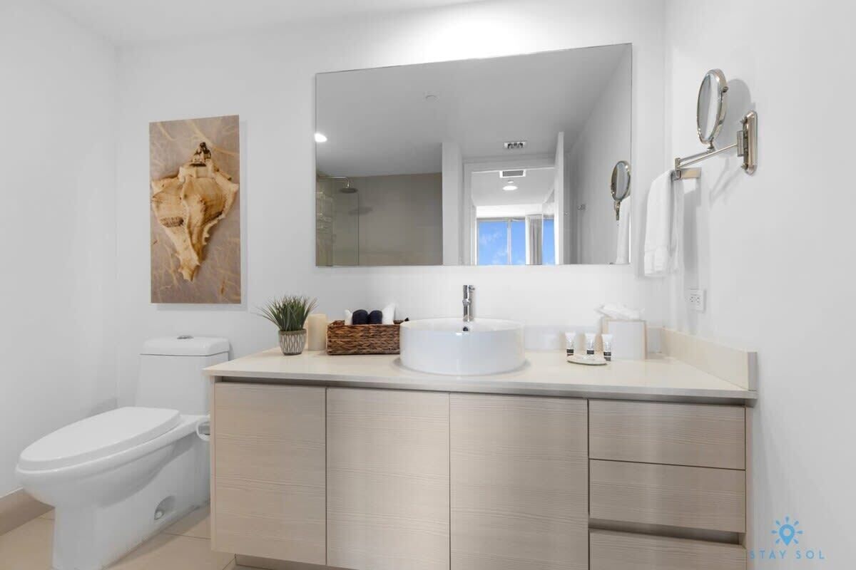 A modern bathroom with a white toilet, a sink with a large mirror, and a decorative piece on the wall.