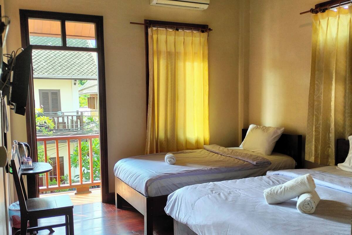 A hotel room with two beds, a wooden ceiling, an air conditioning unit, and a balcony with a view.