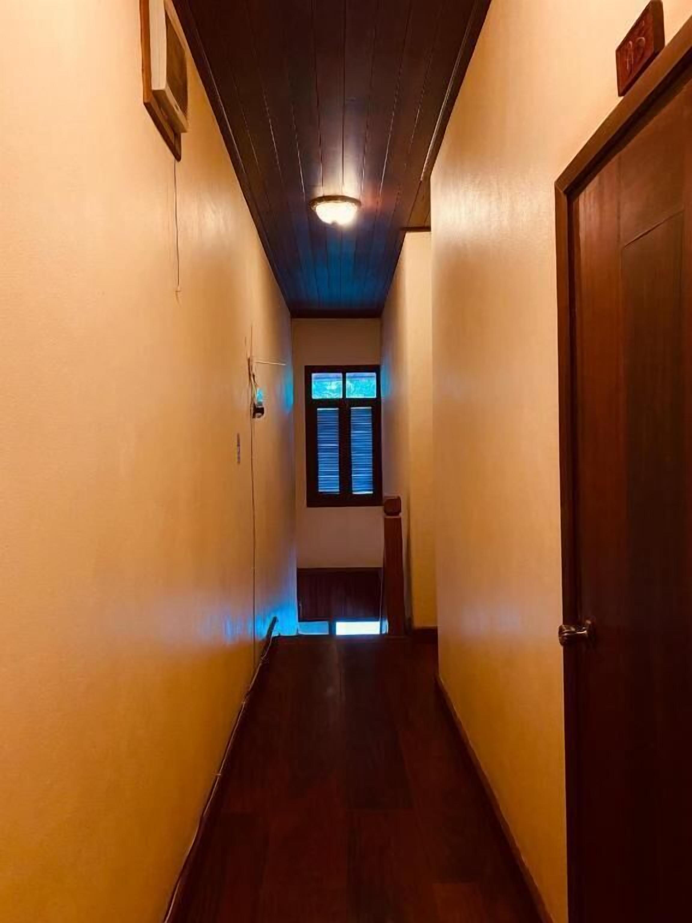 Un estrecho pasillo con suelo y paredes de madera, una lámpara en el techo y una puerta a la derecha.
