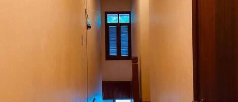 Un estrecho pasillo con suelo y paredes de madera, una lámpara en el techo y una puerta a la derecha.
