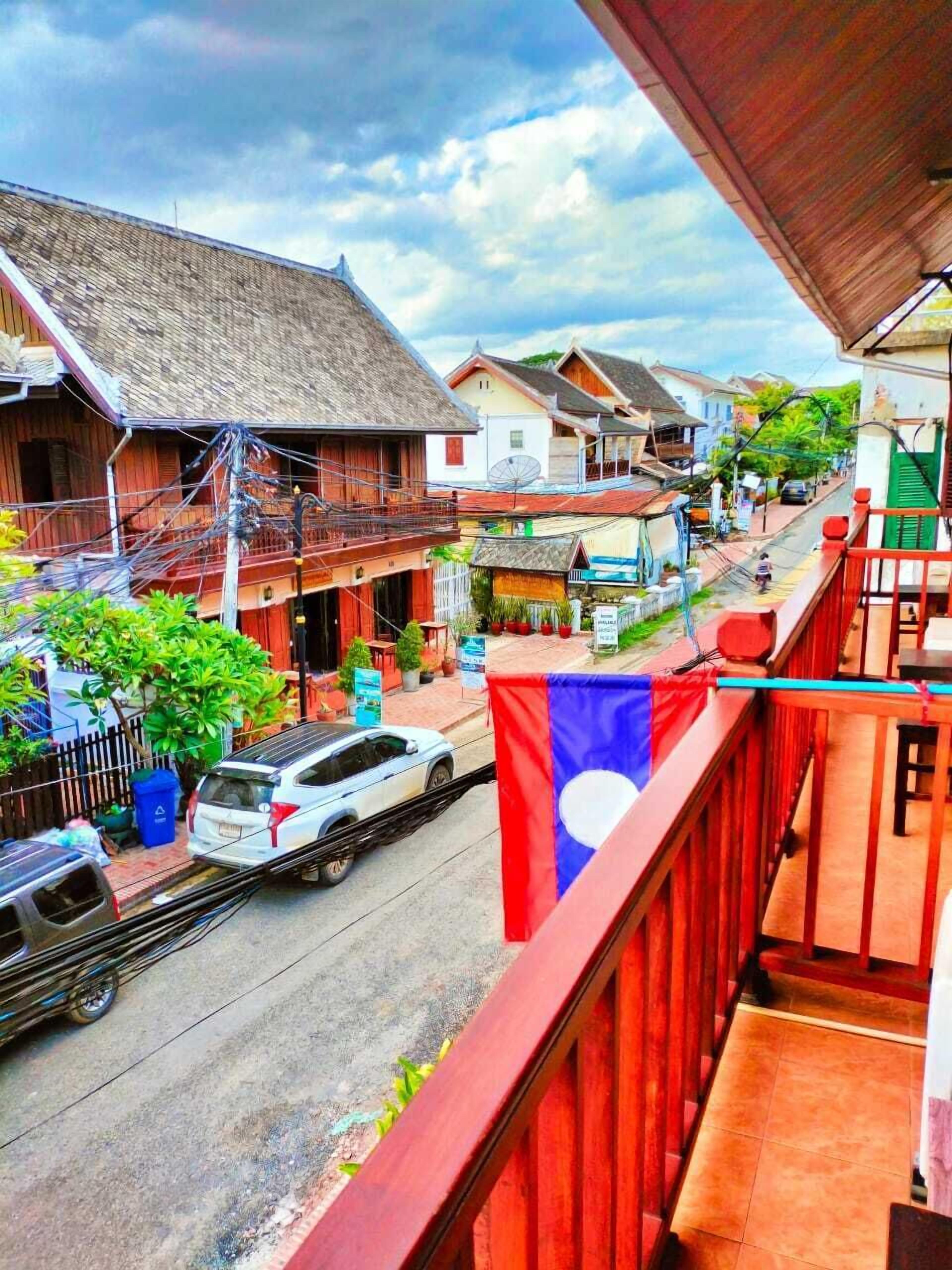 A residential street with houses, a parked car, and a balcony with a flag.