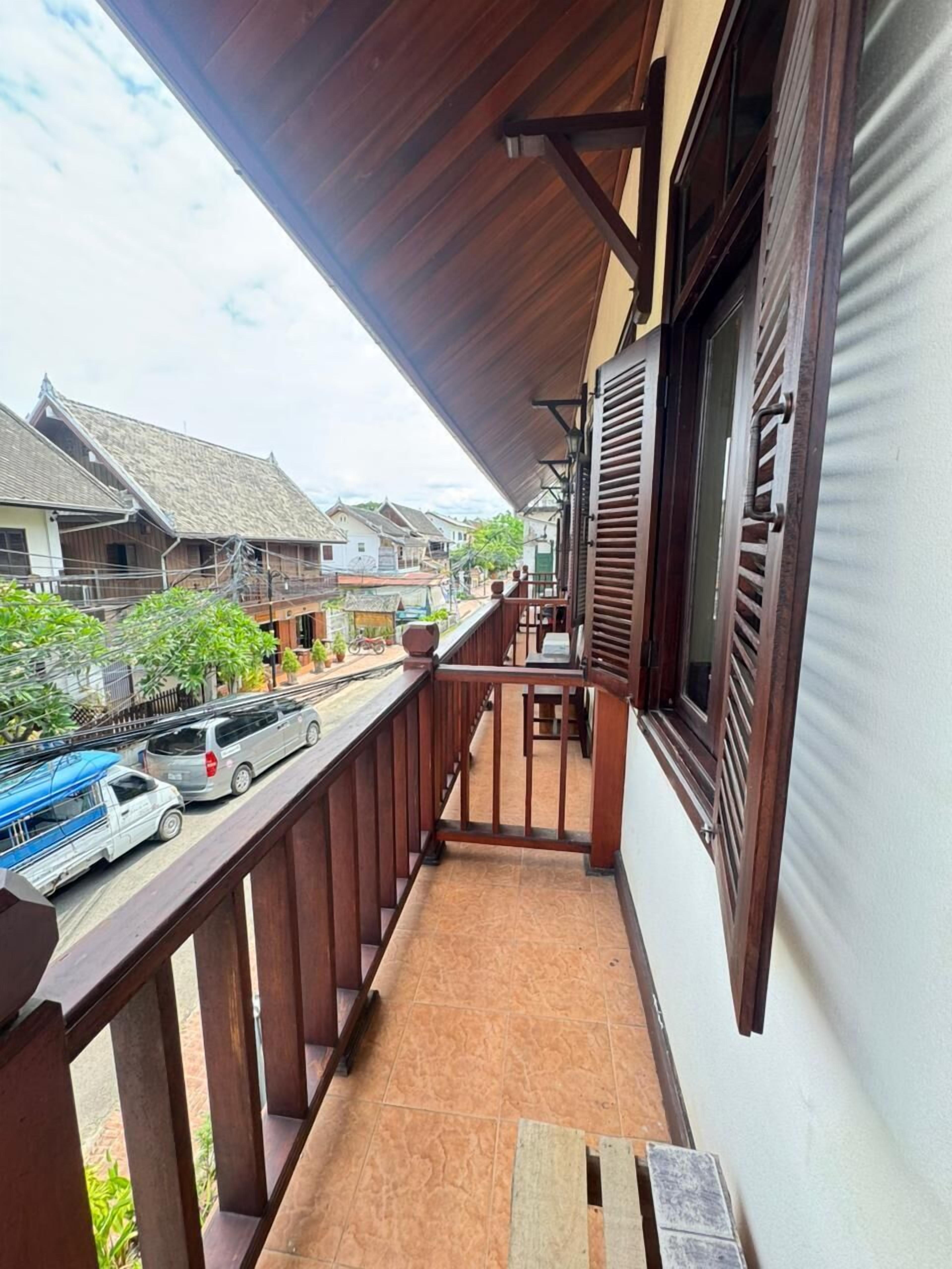 A balcony with a wooden railing, a view of the street, and a building with a traditional roof.