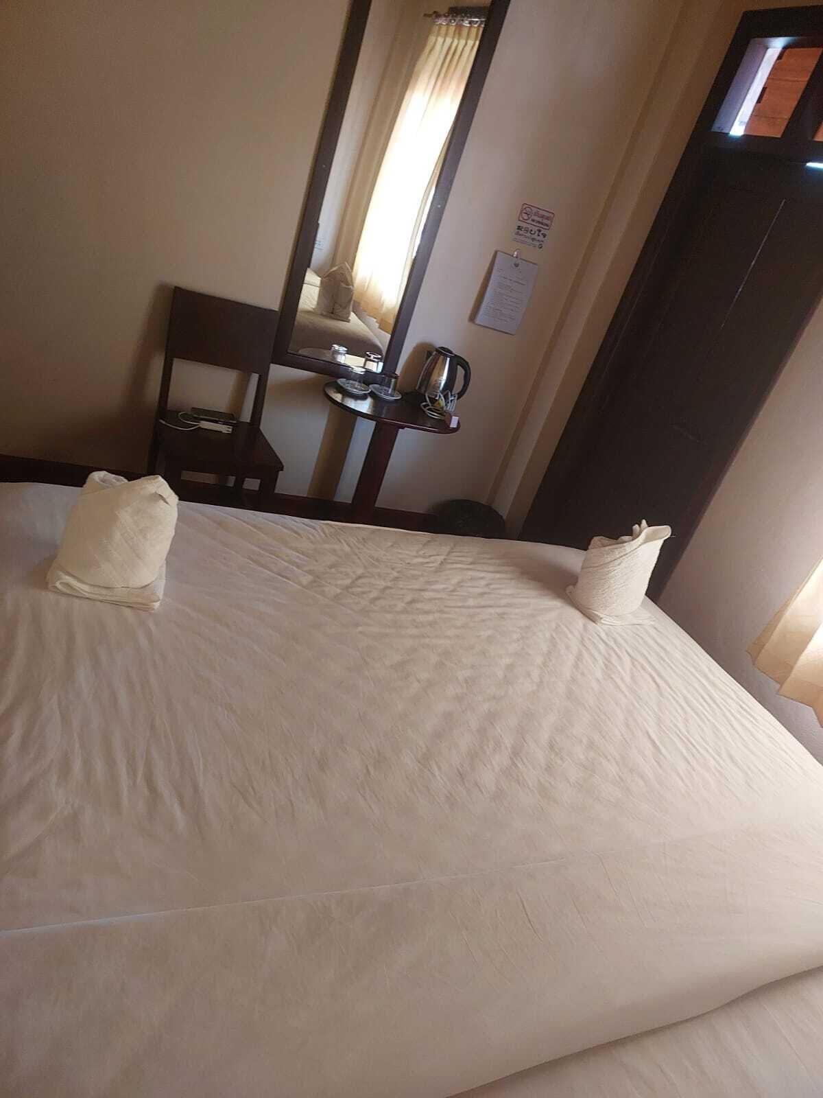 A hotel room with a large bed, a bedside table, a mirror, and a window.