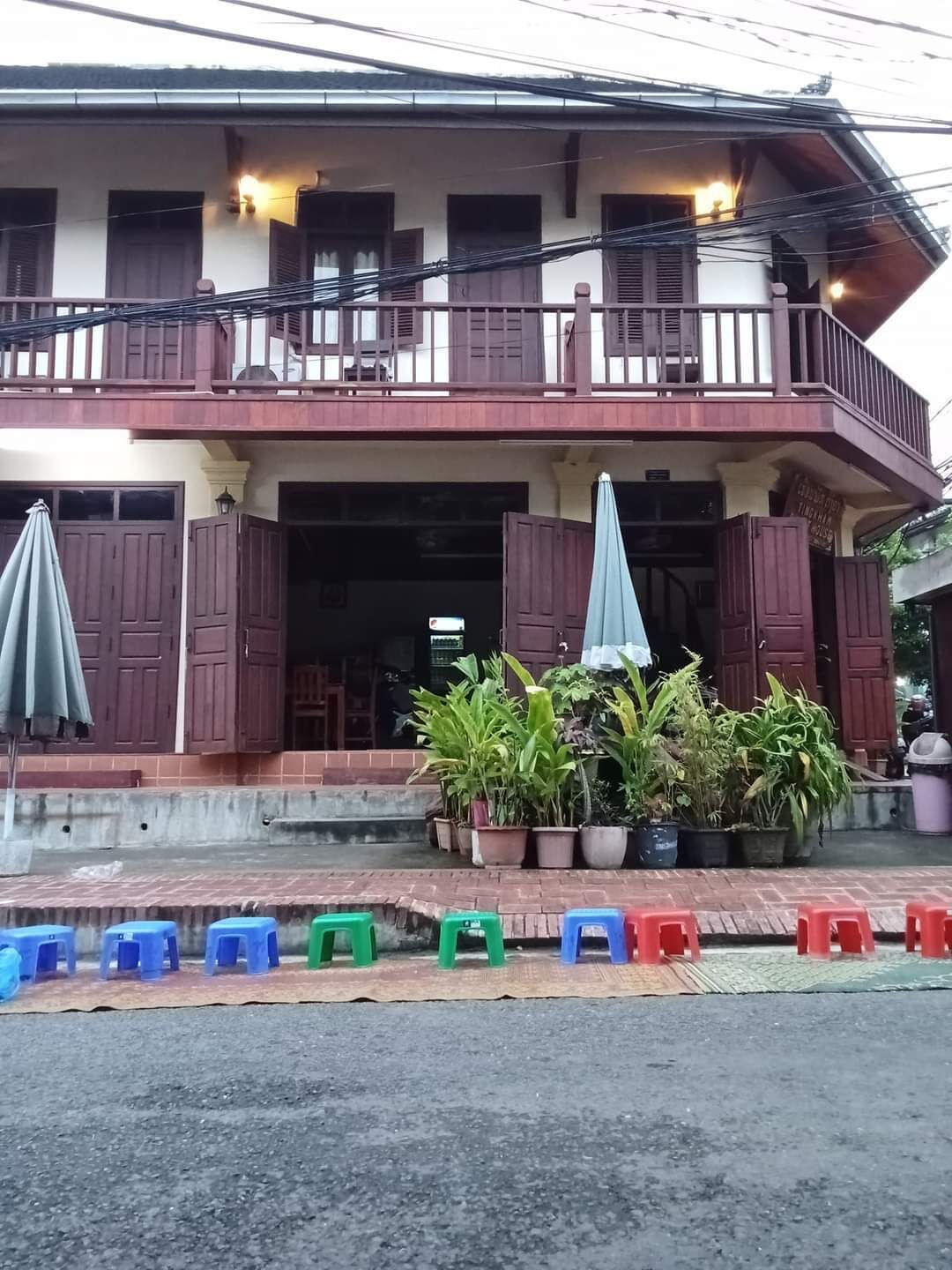 A two-story building with a balcony, potted plants, and a row of colorful plastic stools in front.