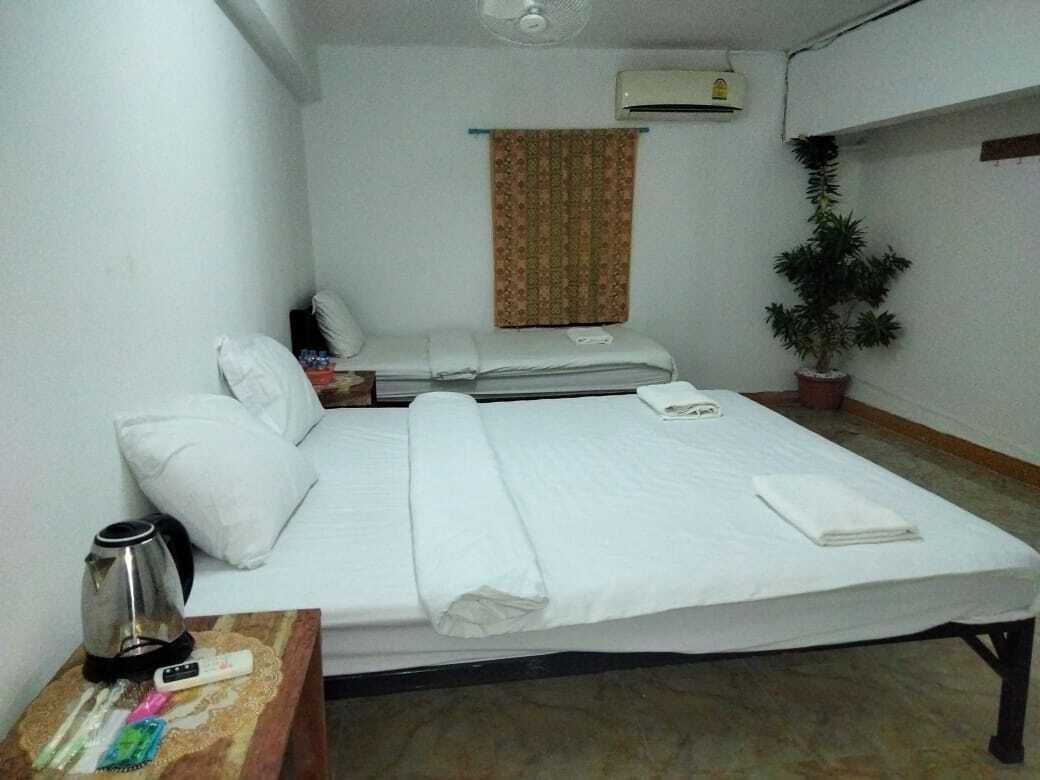 Une chambre avec un lit simple, une table de chevet avec une bouilloire, une plante et un appareil de climatisation fixé au mur.