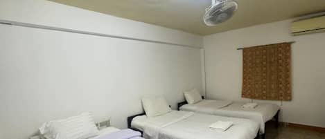 Une chambre avec trois lits, un ventilateur de plafond, un luminaire et une fenêtre avec des rideaux.