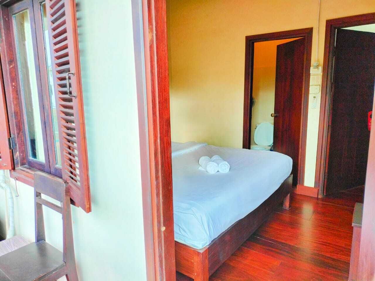 A single bed with a wooden frame and a white mattress, a wooden chair, and a wooden door with a window.