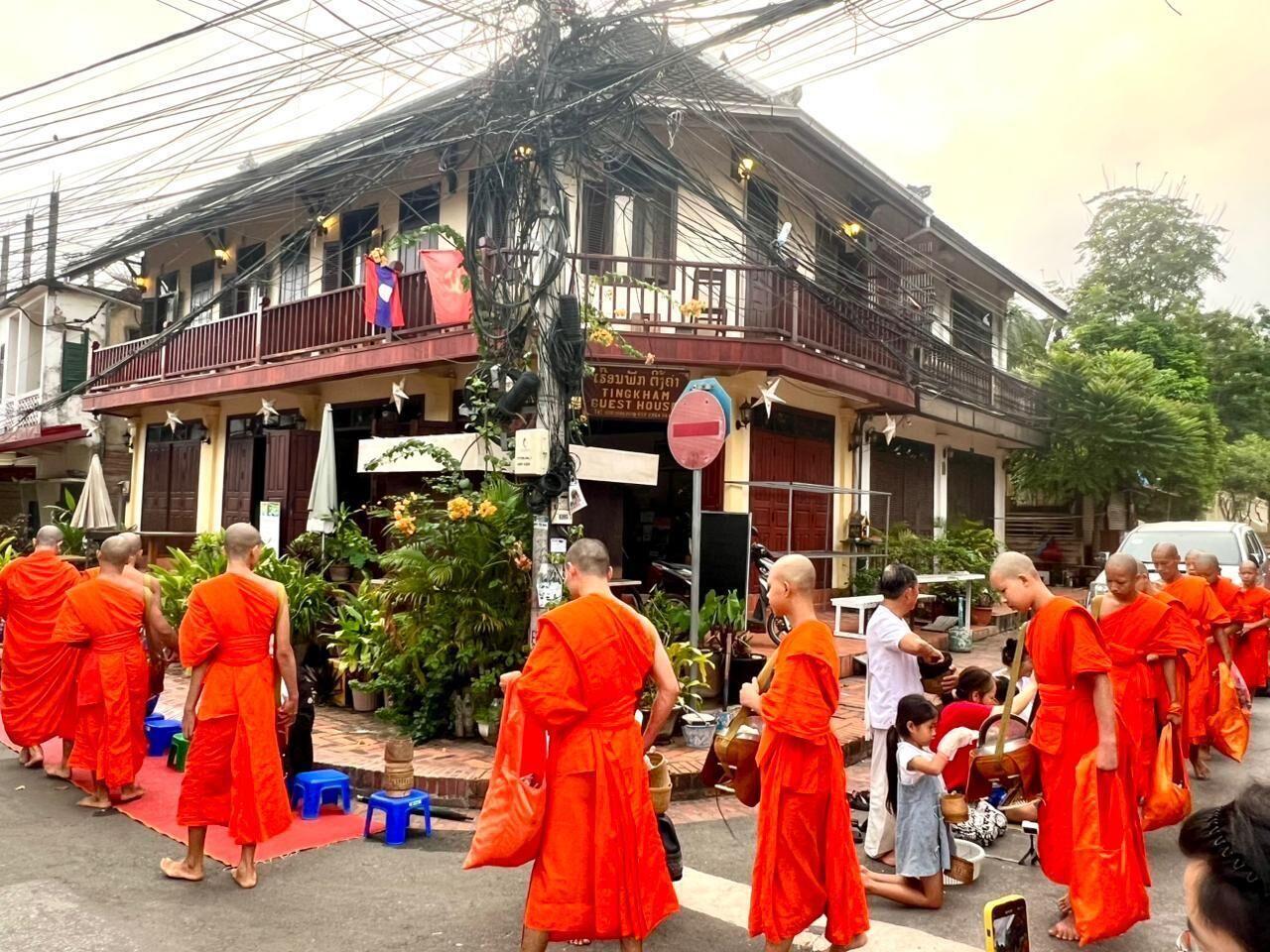 Monjes con túnicas anaranjadas caminando frente a un edificio con un letrero que dice 'Guest House'.
