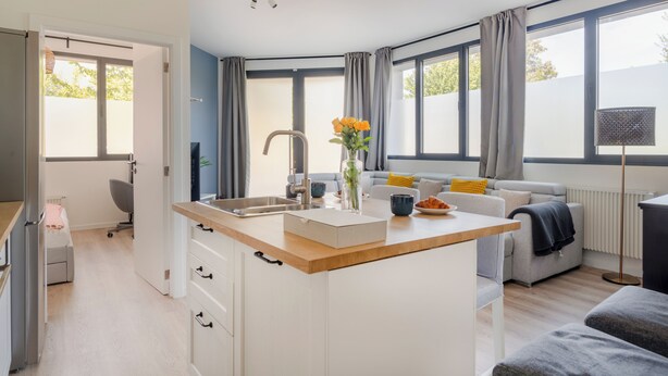 Una cocina moderna con una isla central, un área de comedor con sofá y ventanas amplias.