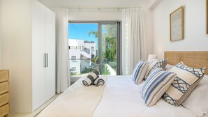 A hotel room with a large bed, white bedding, a view of buildings through a glass door, and a wicker headboard. - Ocean Grand Gaube with LOV (Grand Gaube)